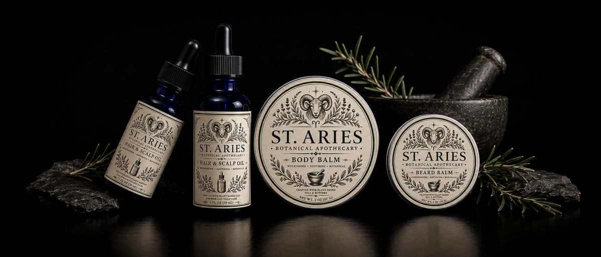 Four St. Aries Apothecary products arranged on a black surface against a black background: two amber dropper bottles, a round tin of beard balm, and a round tin of body balm, styled with rosemary sprigs, dark stones, and a mortar and pestle.